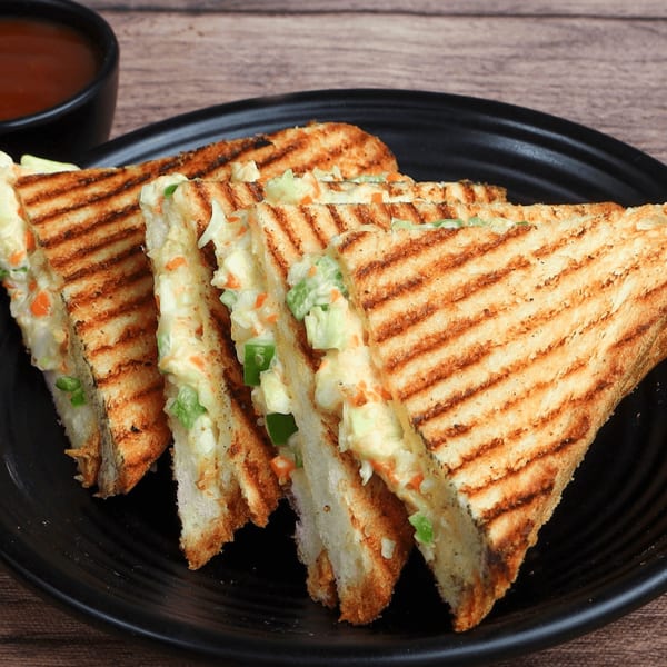 Grilled sandwiches with creamy vegetable filling, served on a black plate with a side of sauce.