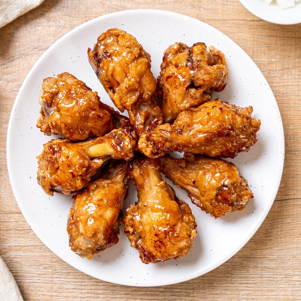 Seven golden-brown glazed chicken drumettes arranged in a circle on a white plate on a wooden table.