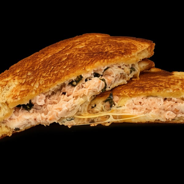A grilled sandwich, cut in half, revealing a creamy salmon and spinach filling with melted cheese.