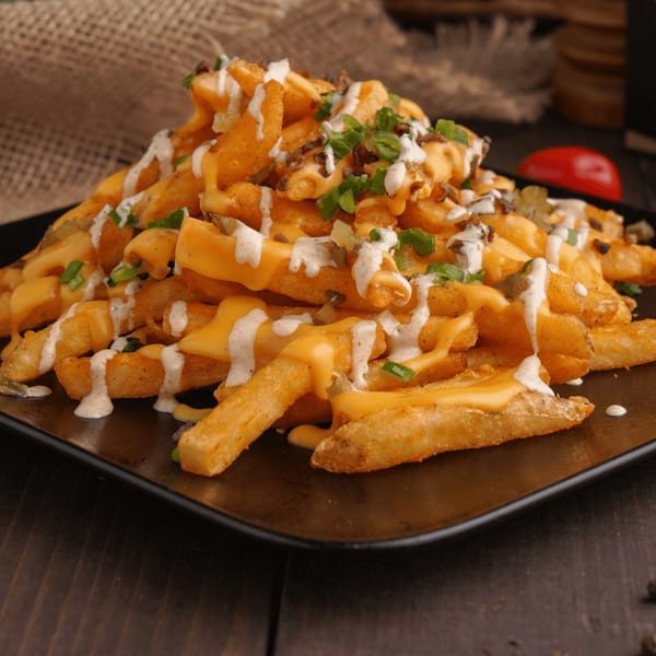 A close-up of golden french fries covered in melted cheese, white sauce, and green onions.