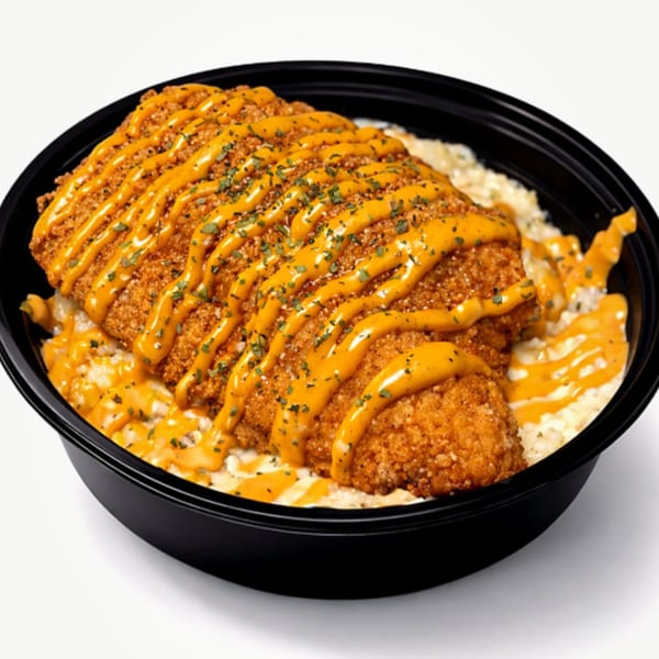 Crispy fried chicken drizzled with orange sauce and herbs, served over grits in a black bowl.