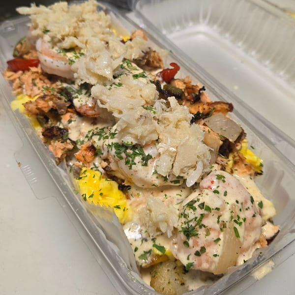 Seafood medley with shrimp, salmon, and crab meat, topped with creamy sauce and parsley in a clear container.